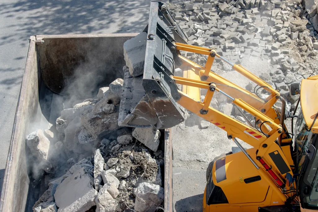 Excavator bucket loading concrete demolition debris into a skip.