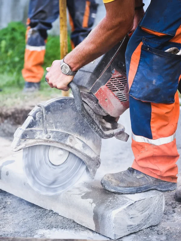 Construction worker cutting concrete or pavement with a circular saw creating dust.